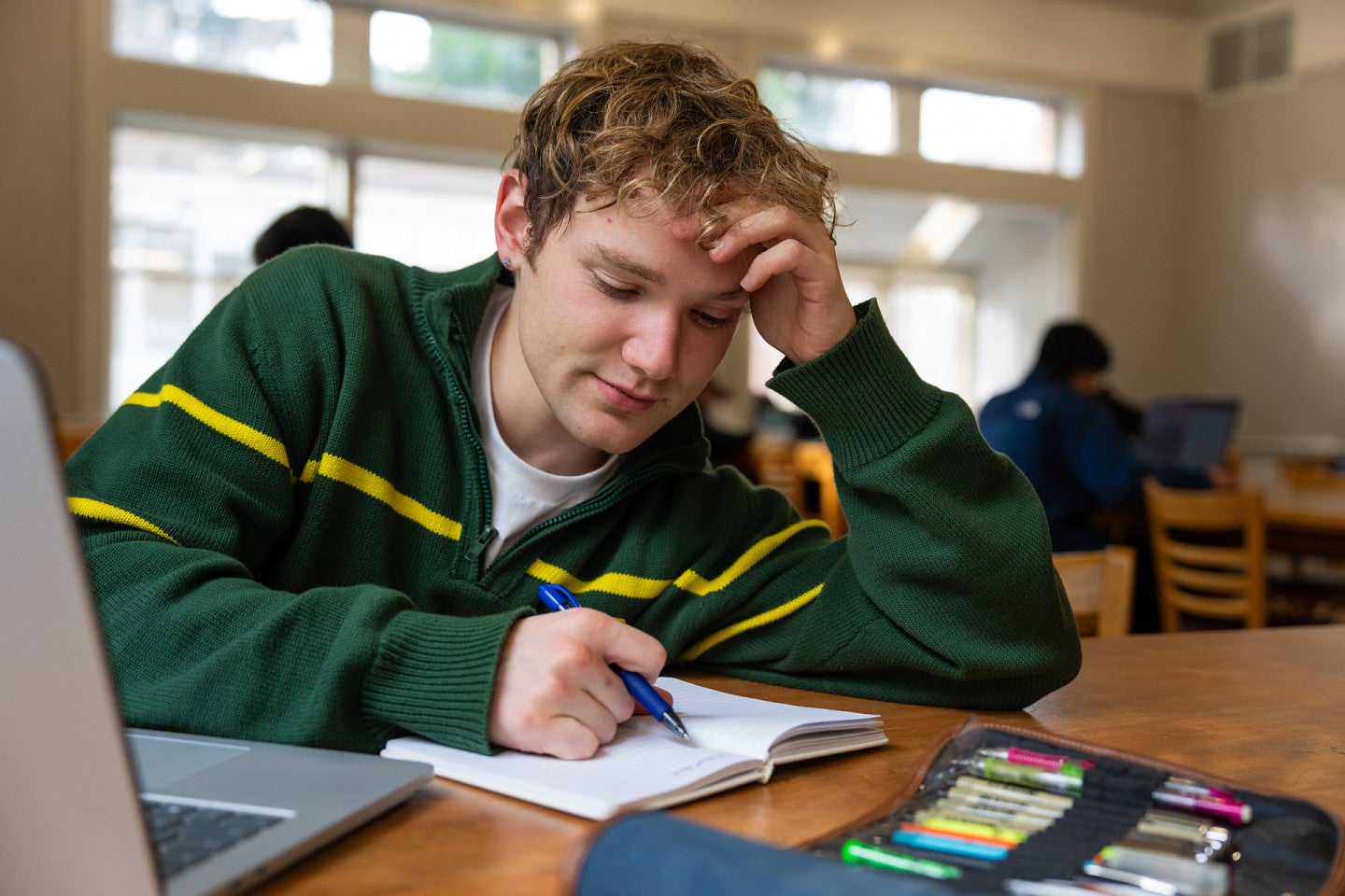 masculine presenting student writing in notebook