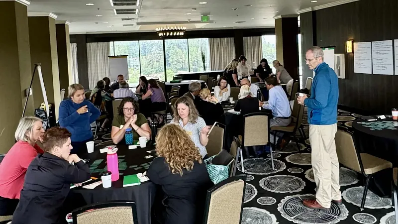 A room with groups of people working on values frameworks at the Office of the Provost Retreat. Provost Long looks on as values are being shared and identified