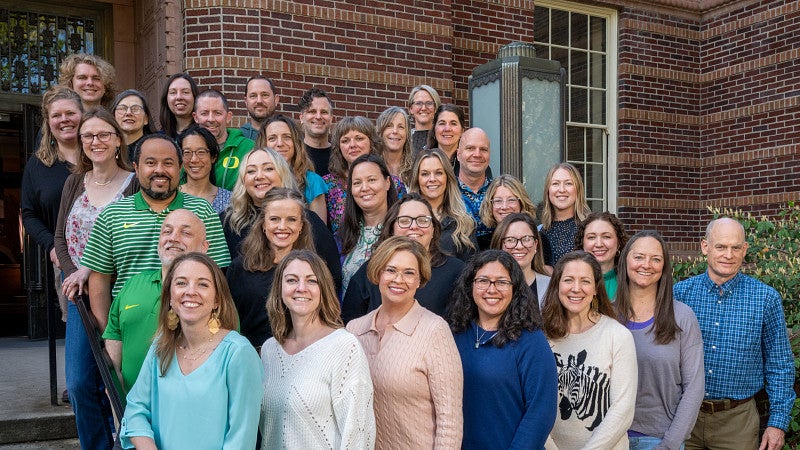 35 people standing together on stairs in front of Knight Library at UO smiling facing forwards