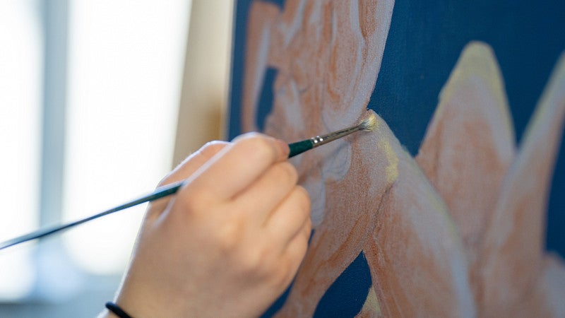 hand holding paintbrush works on piece of art