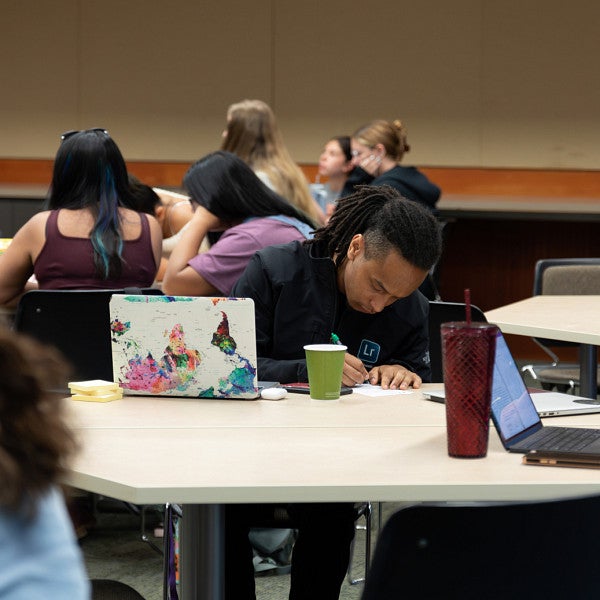 student of color writing on paper at a table during class