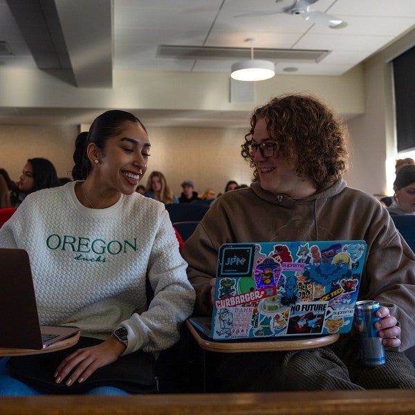 student of color smiles while looking at classmate's laptop screen