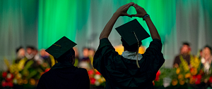 Silhoette of students in regalia throwing the O in front of blurred professors